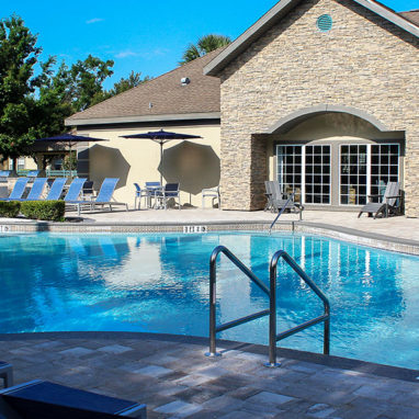 Pool surrounded by lounge chairs with view of clubhouse building in the background