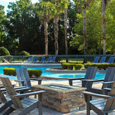 Lounge chairs around a stone firepit next to the pool with trees in the background